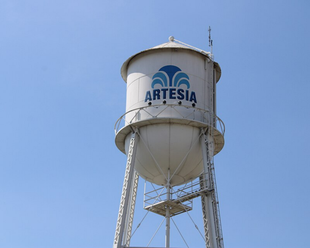 White Artesia water tower on metal supports against a clear blue sky.