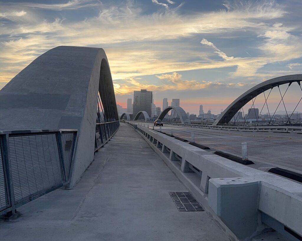 Los Angeles 6th Street Bridge at sunset, with sweeping concrete arches and the downtown skyline in the distance.