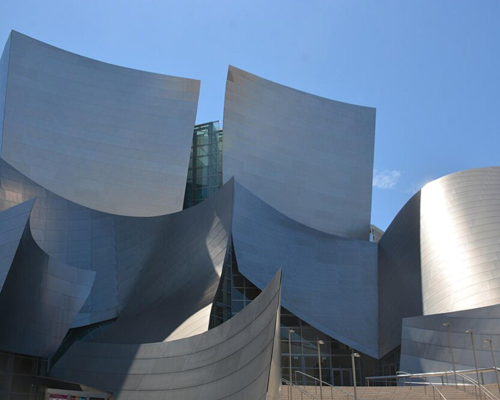 Close-up view of the Walt Disney Concert Hall in Los Angeles, featuring its sweeping curved stainless-steel architecture against a clear blue sky.