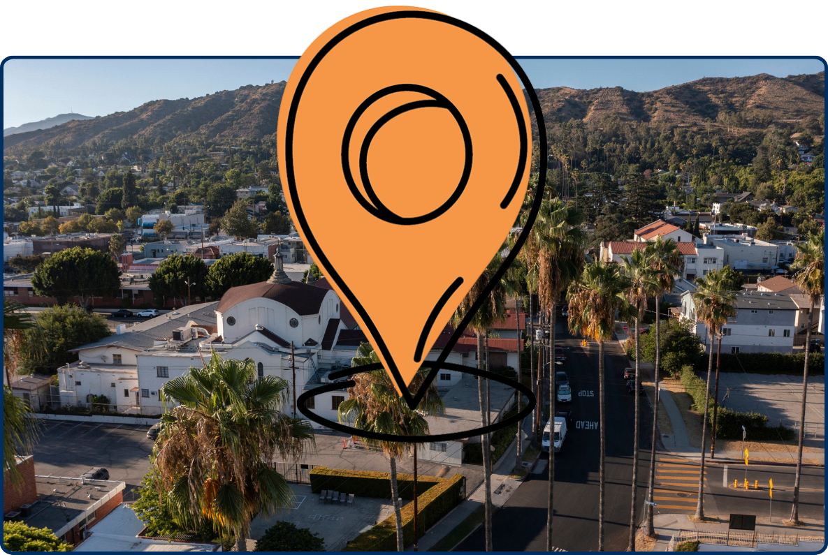 Aerial view of the historic Eagle Rock neighborhood in Los Angeles, with palm trees, residential buildings, and rugged hills in the background.