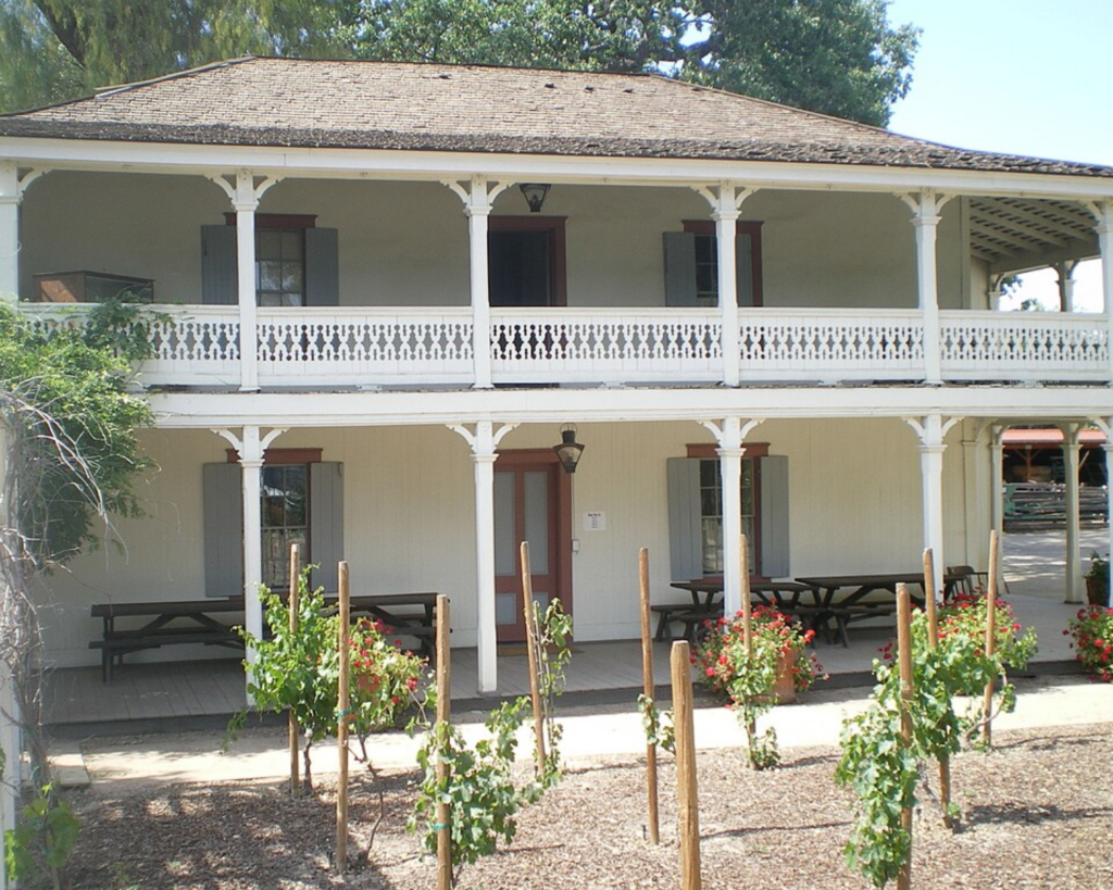 Historic Leonis Adobe in Calabasas, featuring a two-story veranda with decorative railings and a small garden in front.
