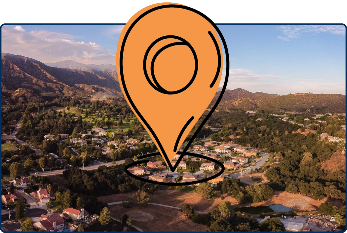 Aerial view of a residential neighborhood and green valley surrounded by rugged mountains under a partly cloudy sky.