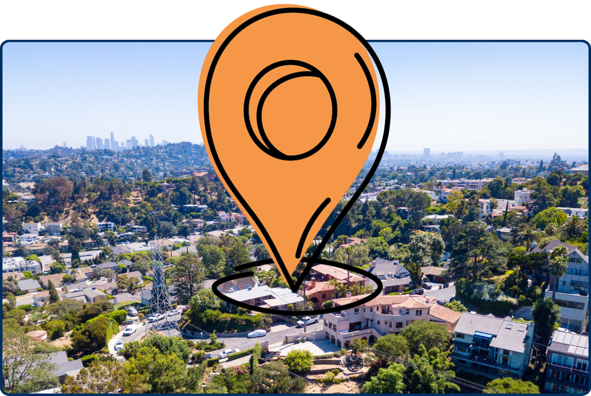 Aerial view of the Los Feliz neighborhood in Los Angeles, with tree-lined residential streets, hillside homes, and the downtown skyline in the distance.