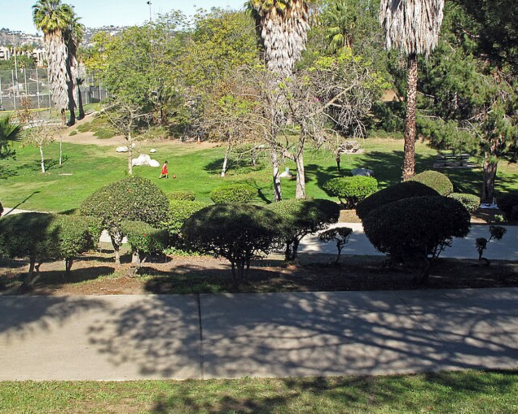 Pan Pacific Park in Los Angeles, featuring green lawns, palm trees, landscaped shrubs, walking paths, and recreational areas.