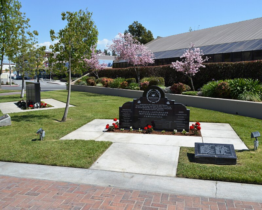 Monterey Park Civic Center grounds with landscaped lawns, flowering trees, memorial plaques, and a civic building in the background.