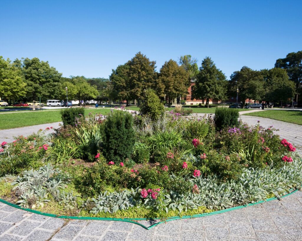Circular flower garden surrounded by paved paths, lawns, and mature trees at Arcade Park in Chicago’s Pullman neighborhood.
