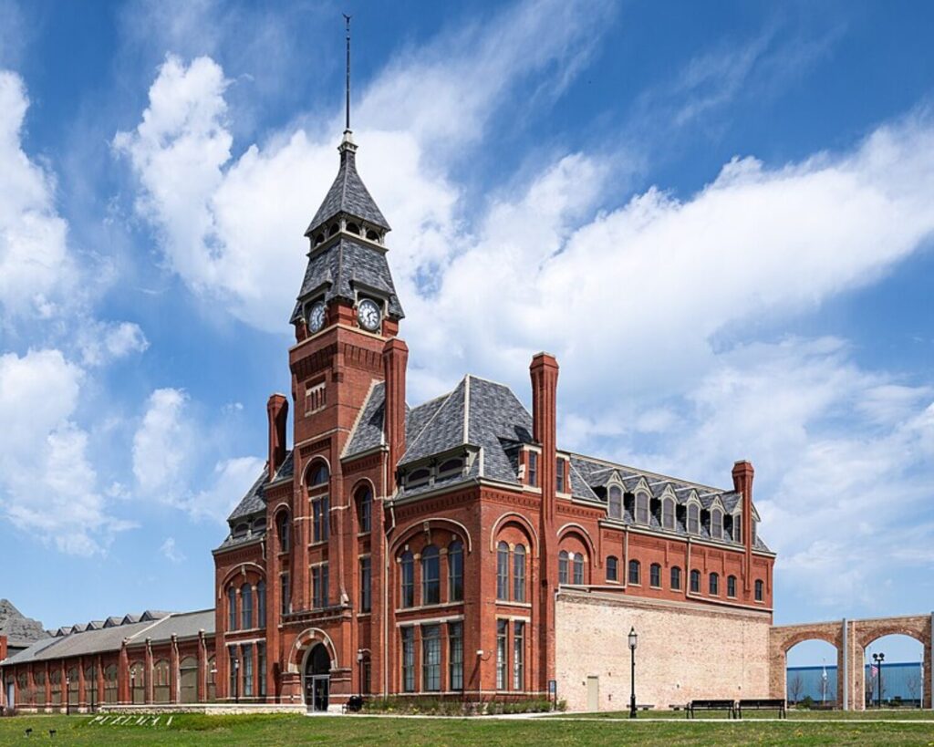Historic red-brick building with a tall clock tower and arched windows under a blue sky.