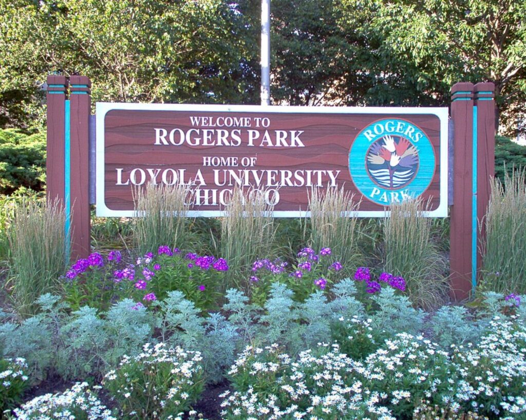 Welcome sign for Rogers Park at Loyola University Chicago, with a circular Rogers Park logo on the right amid plants.
