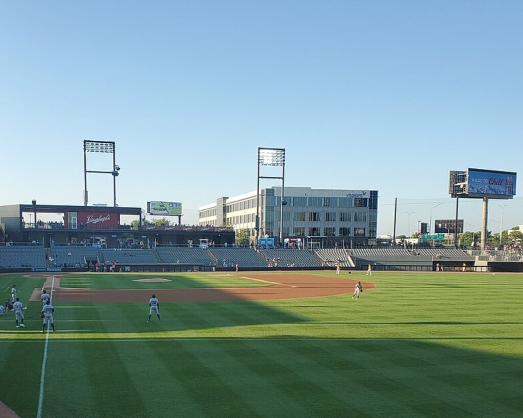 Baseball game at Impact Field with players on the field, spectators in the stands, and buildings beyond the stadium.