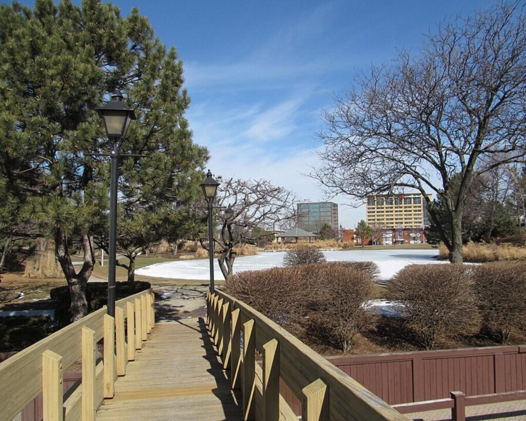 Wooden footbridge with lampposts crossing a snowy park landscape in Rosemont, Illinois.