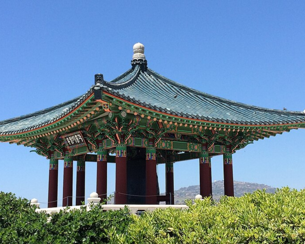 Korean Bell of Friendship pavilion in San Pedro, California, featuring an ornate traditional Korean roof, red columns, and decorative green detailing beneath a clear blue sky.