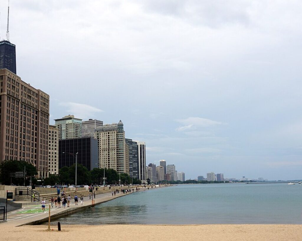 Ohio Street Beach beside Lake Michigan, with pedestrians along the waterfront and Chicago skyscrapers lining the shore.