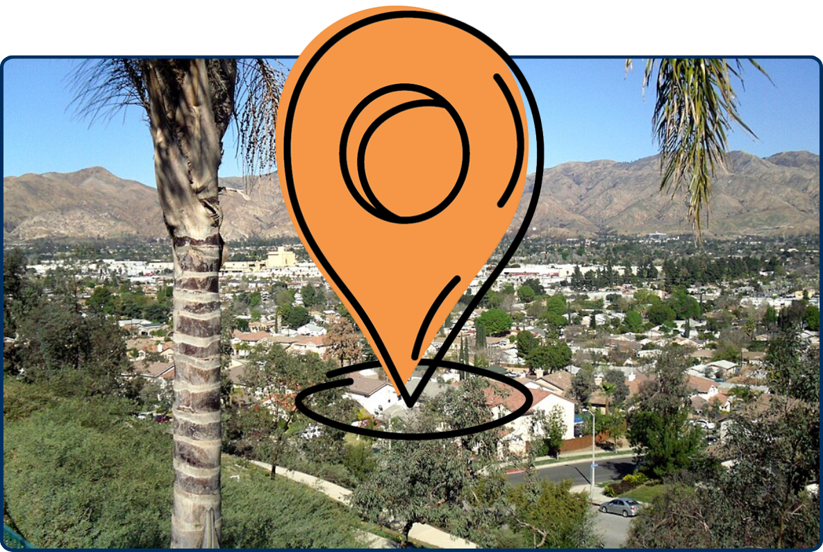 View of Sylmar, Los Angeles, showing residential neighborhoods, palm trees, and rugged mountains under a clear blue sky.