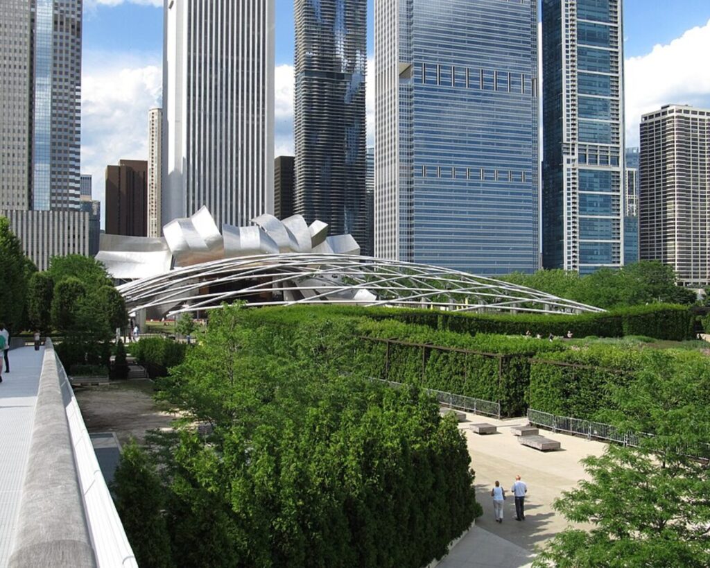 Millennium Park’s Jay Pritzker Pavilion surrounded by greenery and Chicago skyscrapers, viewed from the Nichols Bridgeway.
