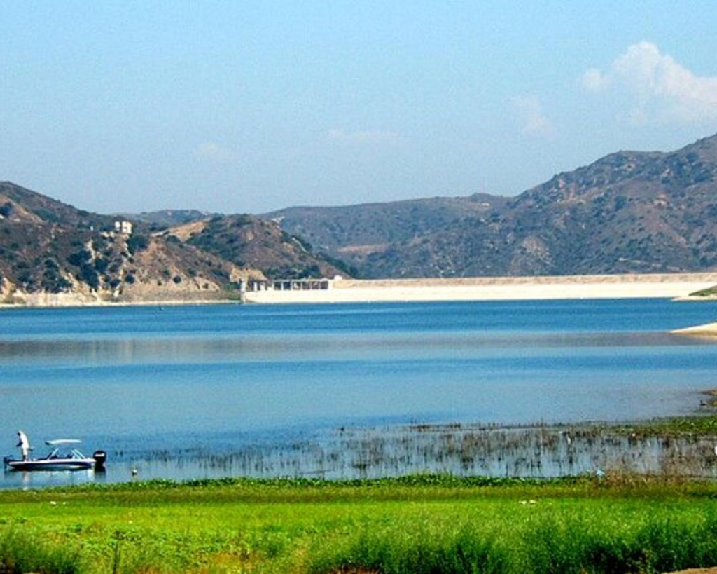 Lake Irvine in California, with calm blue water, green shoreline vegetation, a small boat, and rugged hills in the background.
