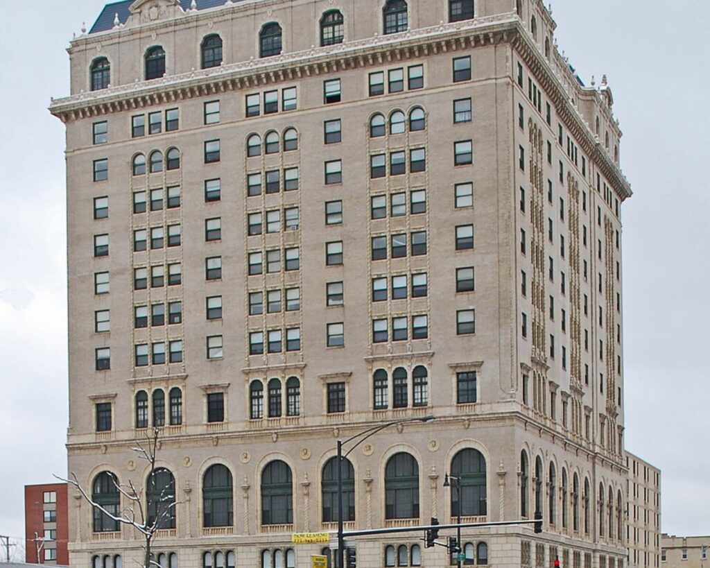 Tall beige historic-style building with arched ground-floor windows and decorative cornice, seen from the street with traffic lights in front