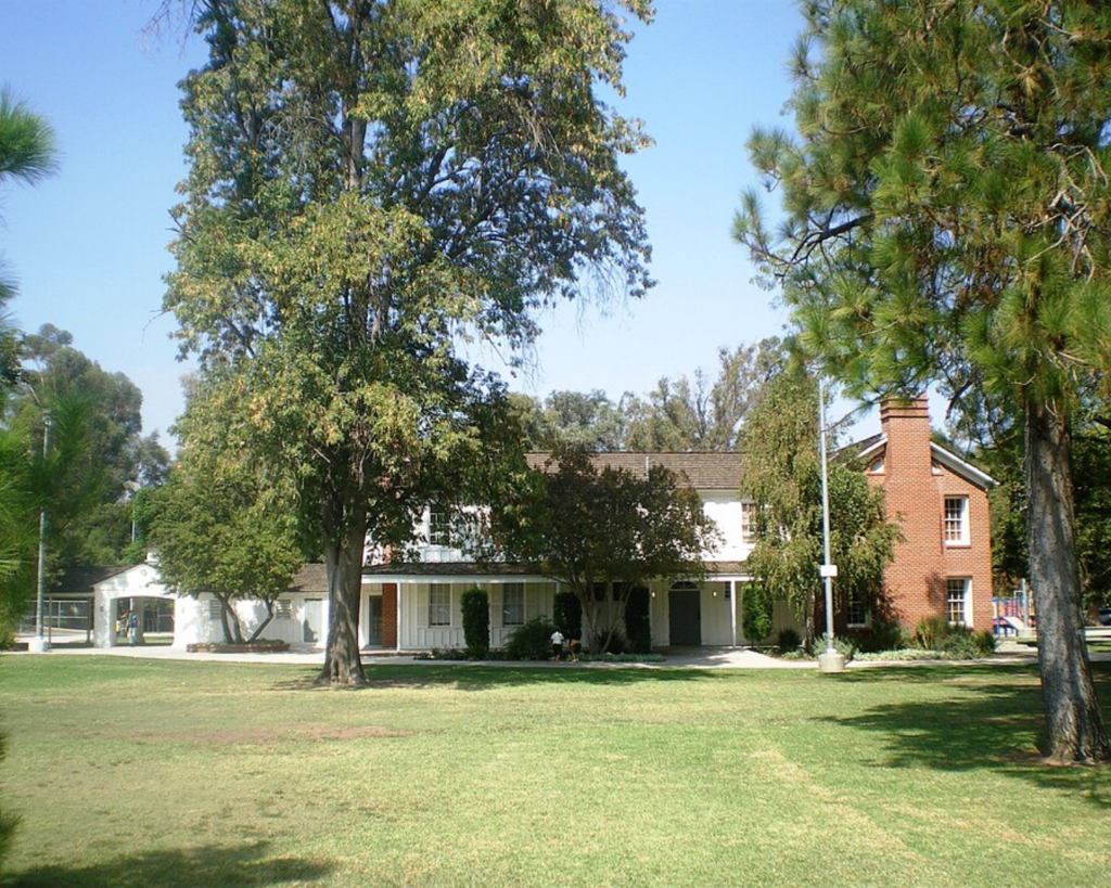 Shadow Ranch in West Hills, Los Angeles, featuring a historic house partially hidden by tall mature trees under a clear blue sky.