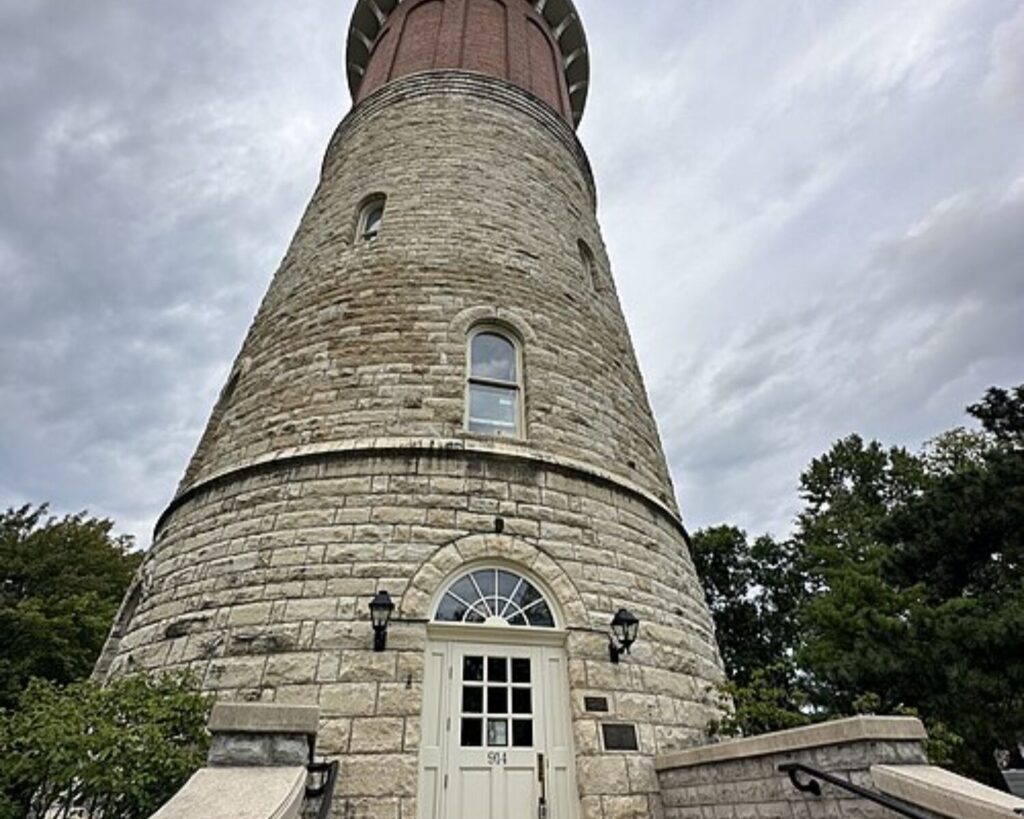 Low-angle view of the historic stone Western Springs Water Tower with its rounded tower and entrance steps under a cloudy sky.
