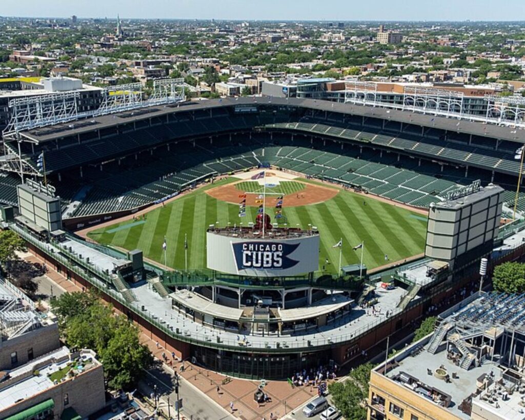 Aerial view of Wrigley Field in Chicago, showing the baseball diamond, grandstands, outfield scoreboard, and surrounding neighborhood.