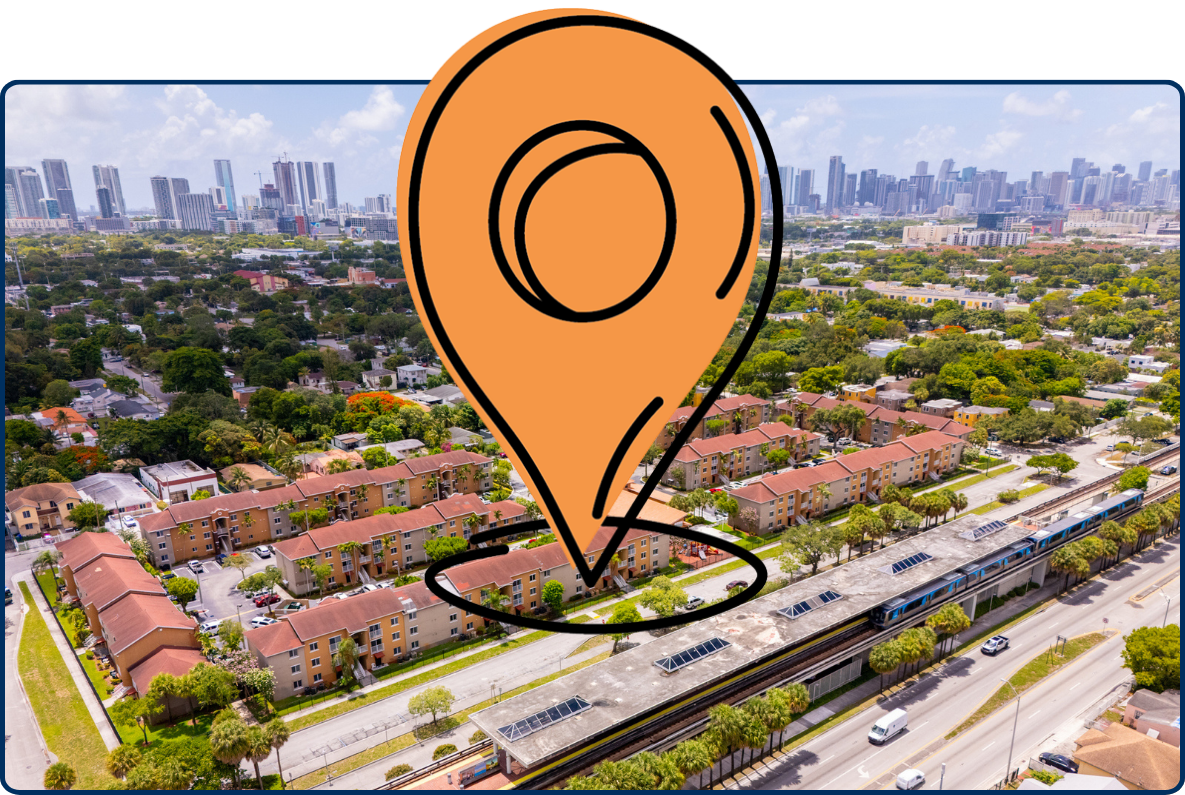 Aerial view of Allapattah in Miami, showing a train station, residential buildings, tree-lined neighborhoods, roads, and the downtown skyline in the distance.