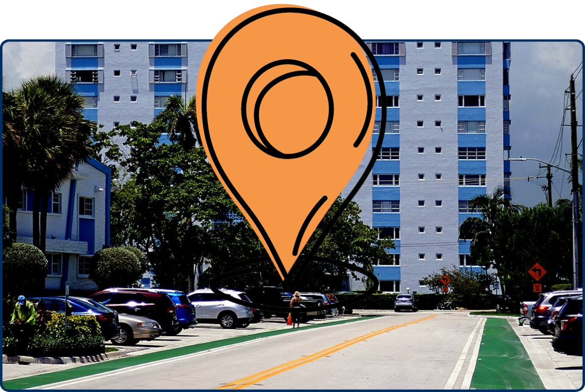 Street view in Bay Harbor Islands, Miami, with a mid-rise residential building, parked cars, palm trees, bike lanes, and large clouds overhead.