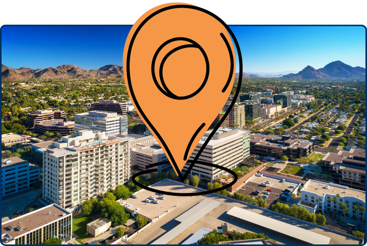 Aerial view of the Biltmore neighborhood in Phoenix, Arizona, showing modern office and residential buildings surrounded by green neighborhoods and rugged desert mountains under a clear blue sky.
