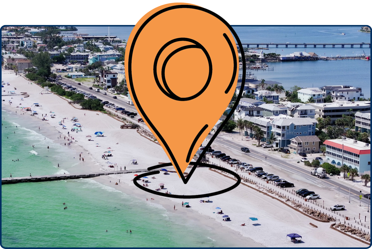 Aerial view of Bradenton Beach on Anna Maria Island, Florida, showing beachgoers along the white sandy shoreline, turquoise Gulf water, a coastal road, homes, and bridges over nearby waterways.