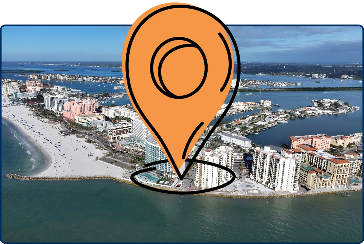 Aerial view of Clearwater Beach, Florida, showing a broad sandy shoreline, blue-green Gulf waters, beachfront hotels, and high-rise buildings along the coast.