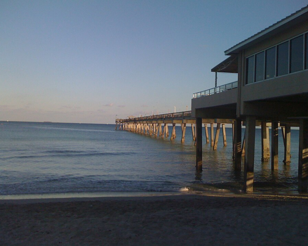Dania Beach pier in Florida extending over calm ocean water beside a sandy shoreline at dusk.