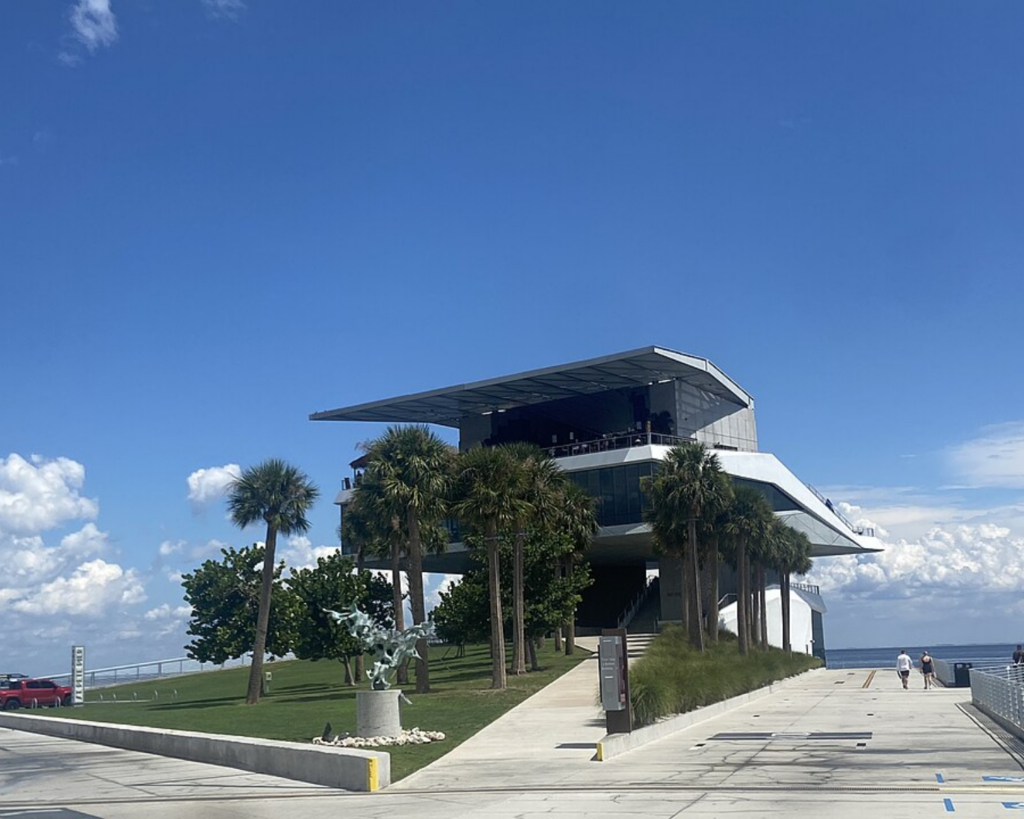 Pier Point building at St. Pete Pier in St. Petersburg, Florida, featuring modern waterfront architecture, palm trees, landscaped lawns, and a clear blue sky.