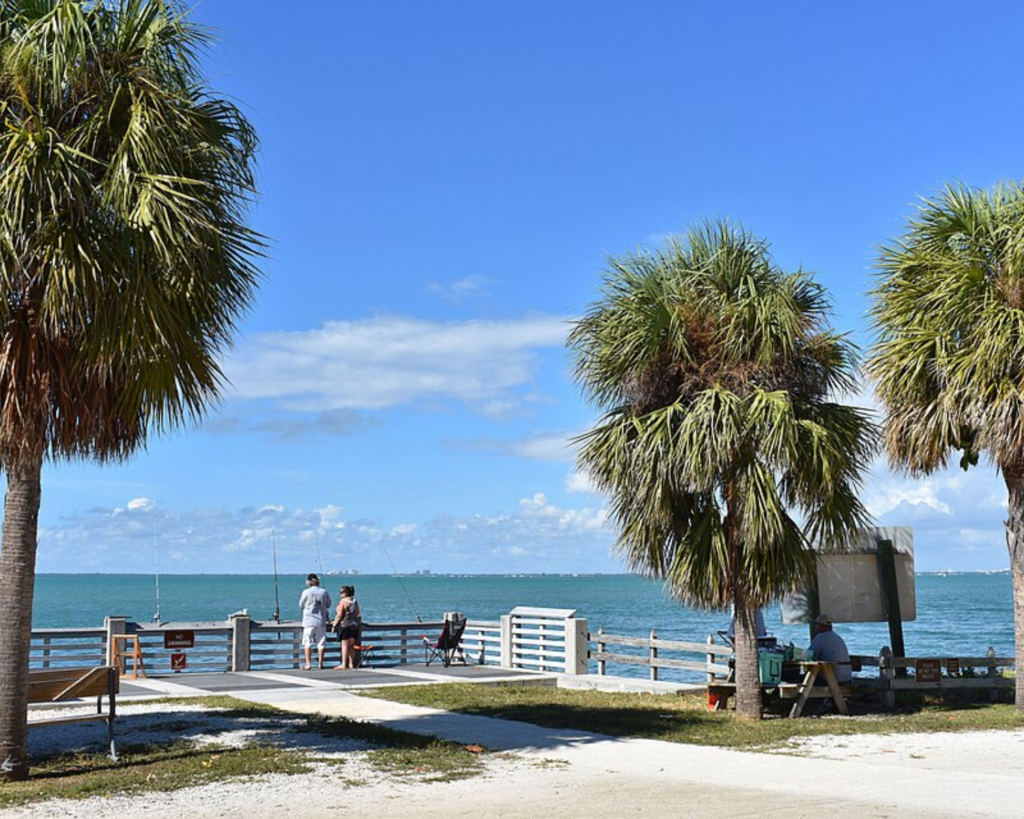 Bill Baggs Cape Florida State Park in Key Biscayne, Florida, with palm trees, a waterfront pier, and visitors overlooking the blue ocean.