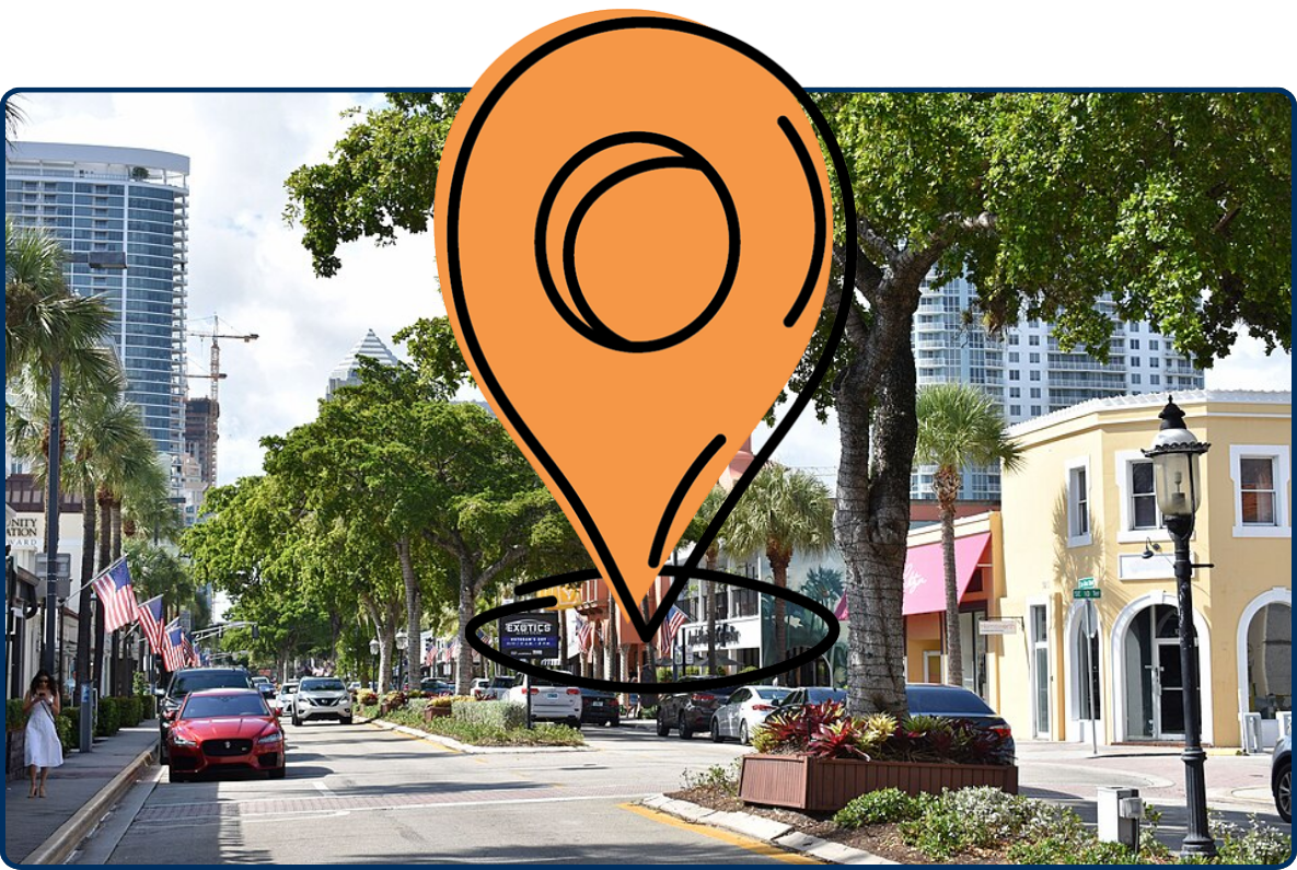 Las Olas Boulevard in Fort Lauderdale, Florida, lined with shops, palm trees, large shade trees, parked cars, and modern high-rise buildings in the background.