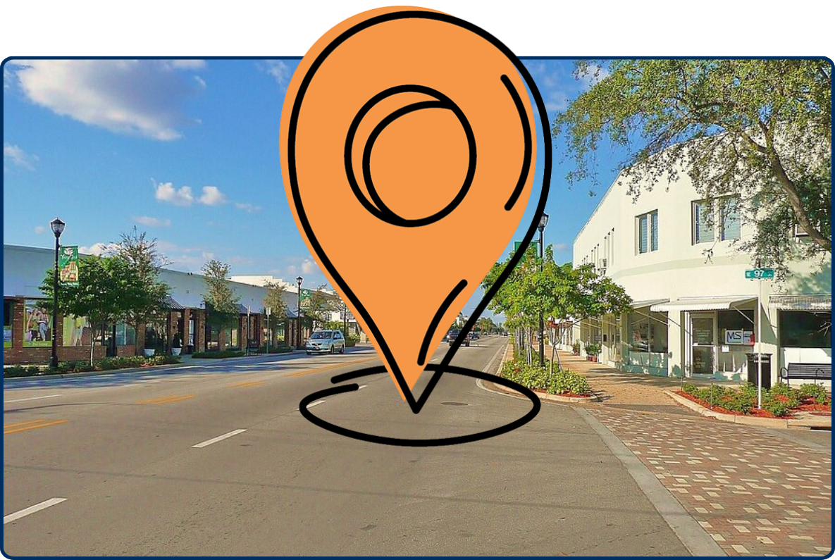 Downtown Miami Shores, Florida, showing a wide street lined with low-rise shops, trees, sidewalks, and a few cars under a blue sky.