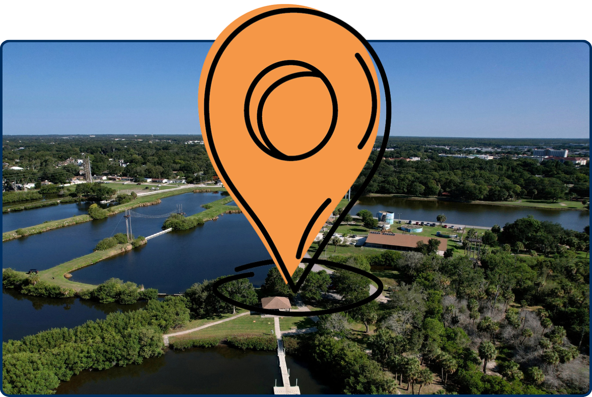 Aerial view of Oldsmar, Florida, showing ponds, green parkland, walking paths, a waterfront pier, and surrounding residential areas under a clear blue sky.