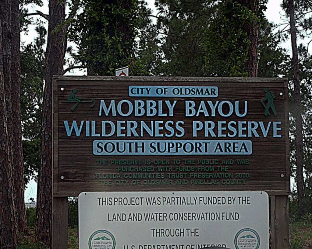 Entrance sign for Mobbly Bayou Wilderness Preserve in Oldsmar, Florida, surrounded by tall trees and dense woodland.