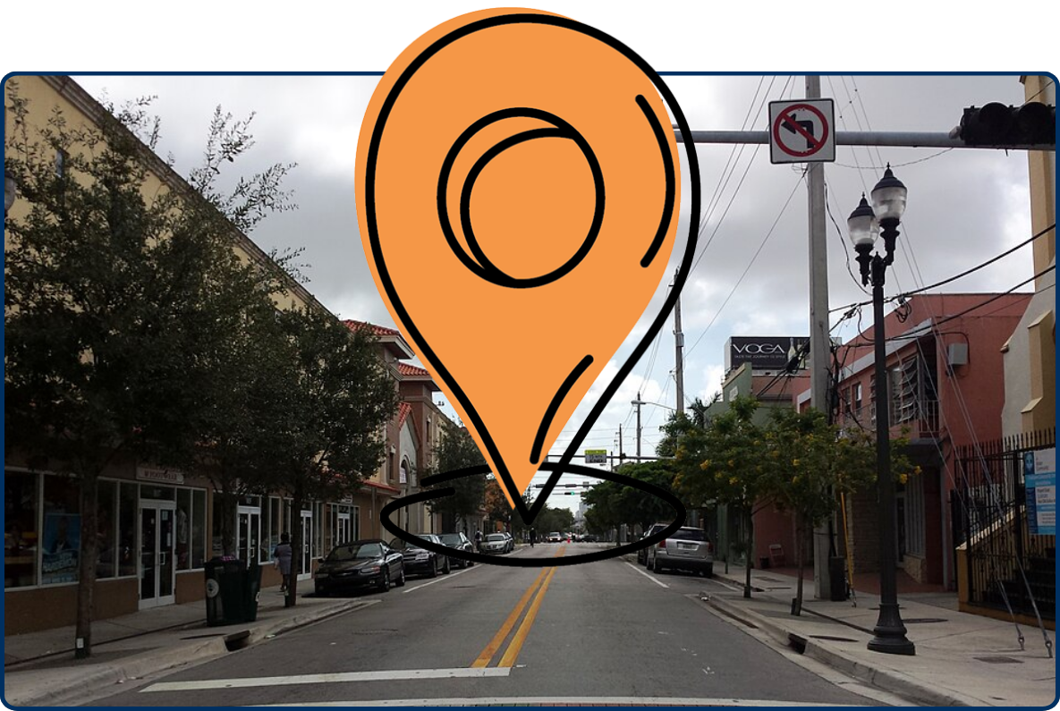 Street view of NW 3rd Avenue in Miami’s Overtown neighborhood, with parked cars, storefronts, traffic lights, decorative street lamps, and a colorful patterned crosswalk.