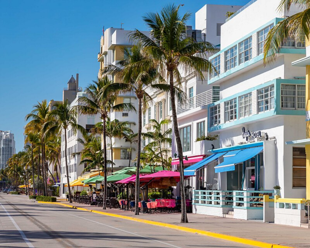 Ocean Drive in Miami Beach’s Art Deco Historic District, lined with colorful Art Deco buildings, palm trees, outdoor cafés, and a wide sunlit street.