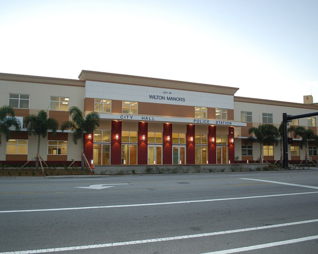 Wilton Manors City Hall and Police Station in Florida, with palm trees, illuminated entrances, and a wide roadway in front.