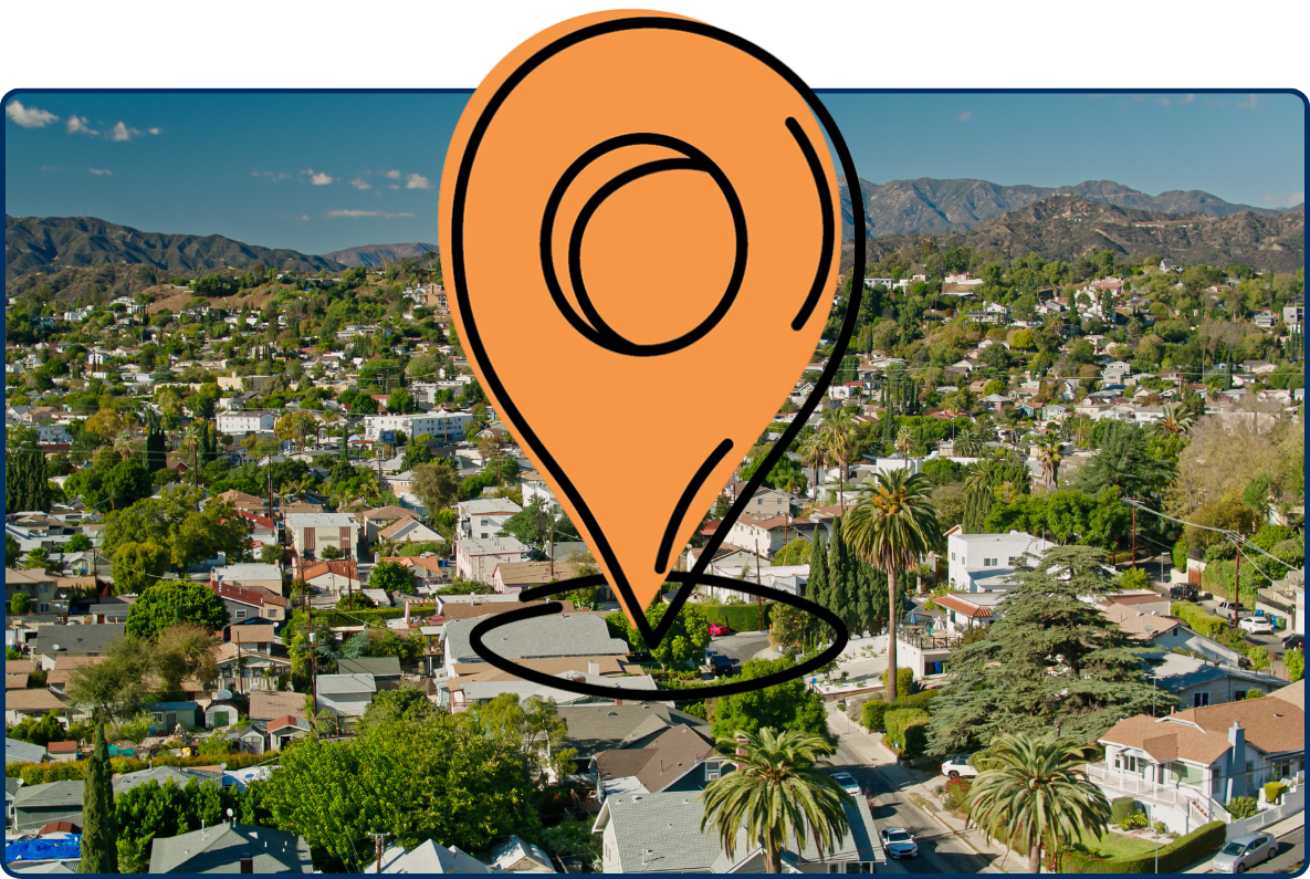 Aerial view of Highland Park in Los Angeles, California, showing a dense residential neighborhood with palm trees and green foliage, backed by rugged mountains under a clear blue sky.
