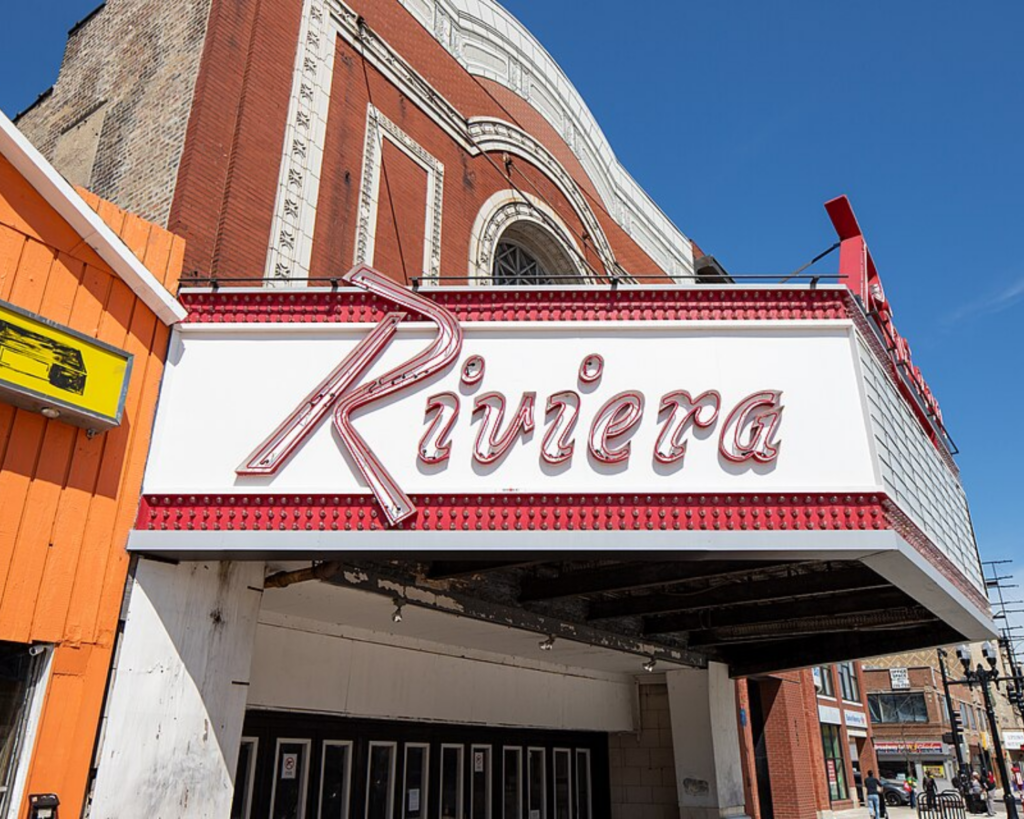 Riviera Theatre in Chicago, Illinois, featuring its large vintage marquee and ornate red-brick facade beneath a clear blue sky.